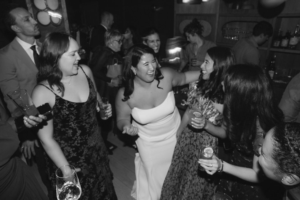 Black and White Image of Bride in Strapless Dress Dancing With Guests With Cocktails