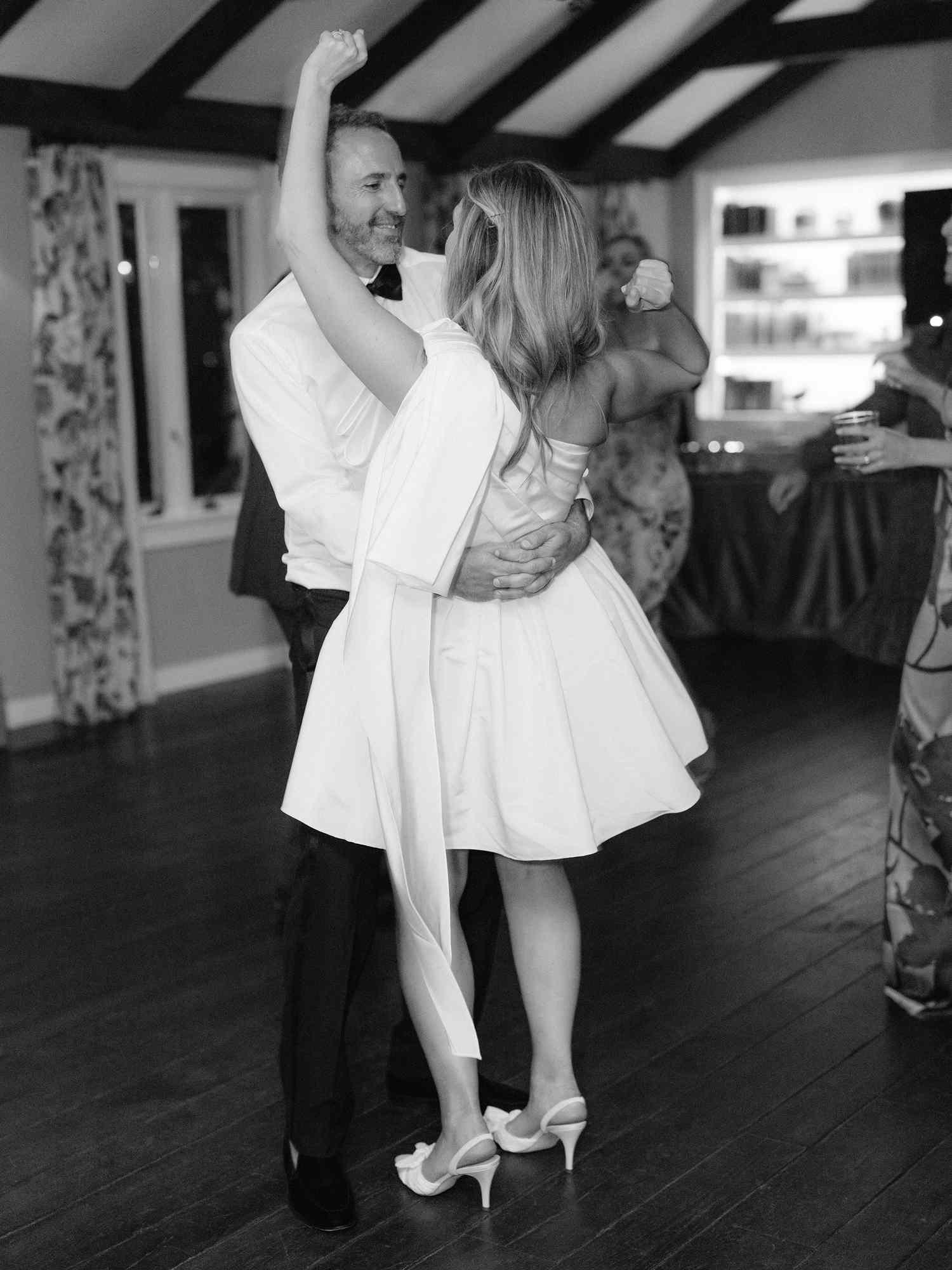 black and white photo of bride in short white dress dancing with groom