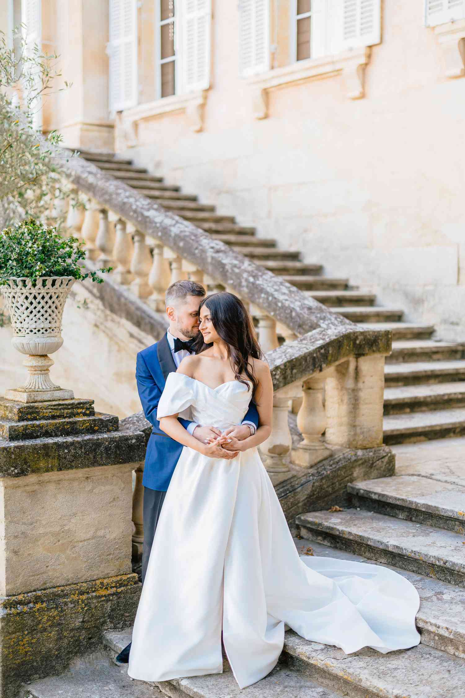 bride in white dress and groom in navy suit holding one another on the staircase