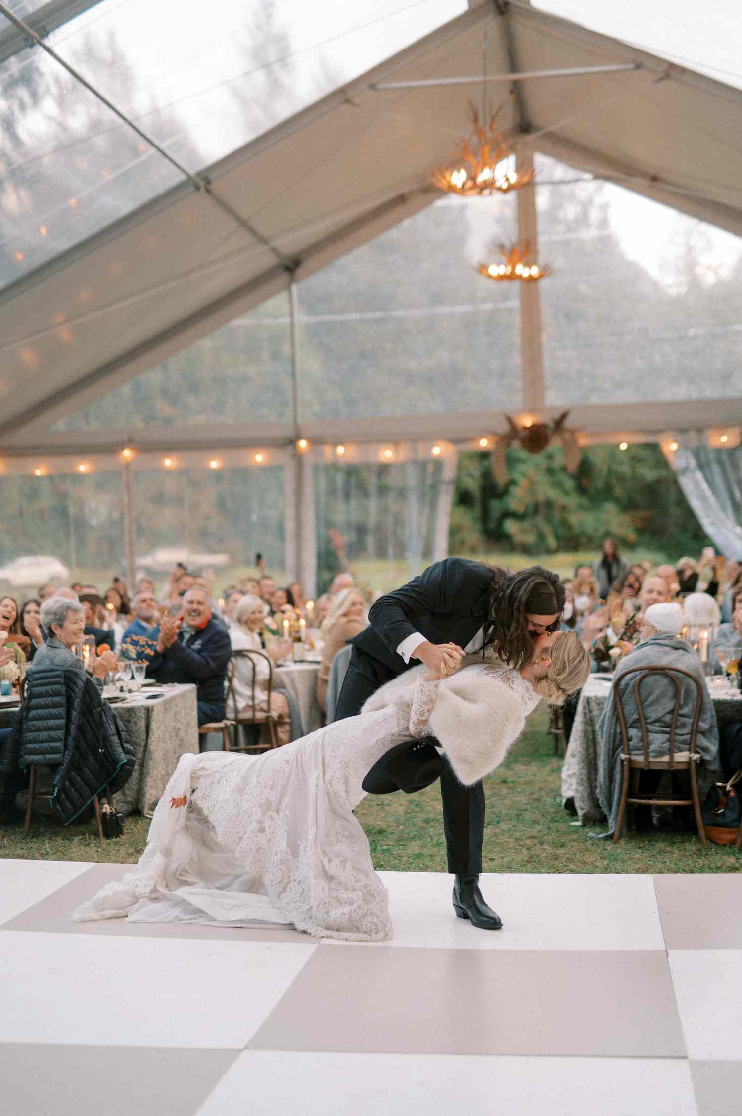 Bride in Lace Wedding Dress Kissing Groom in Black Tuxedo on Dance Floor