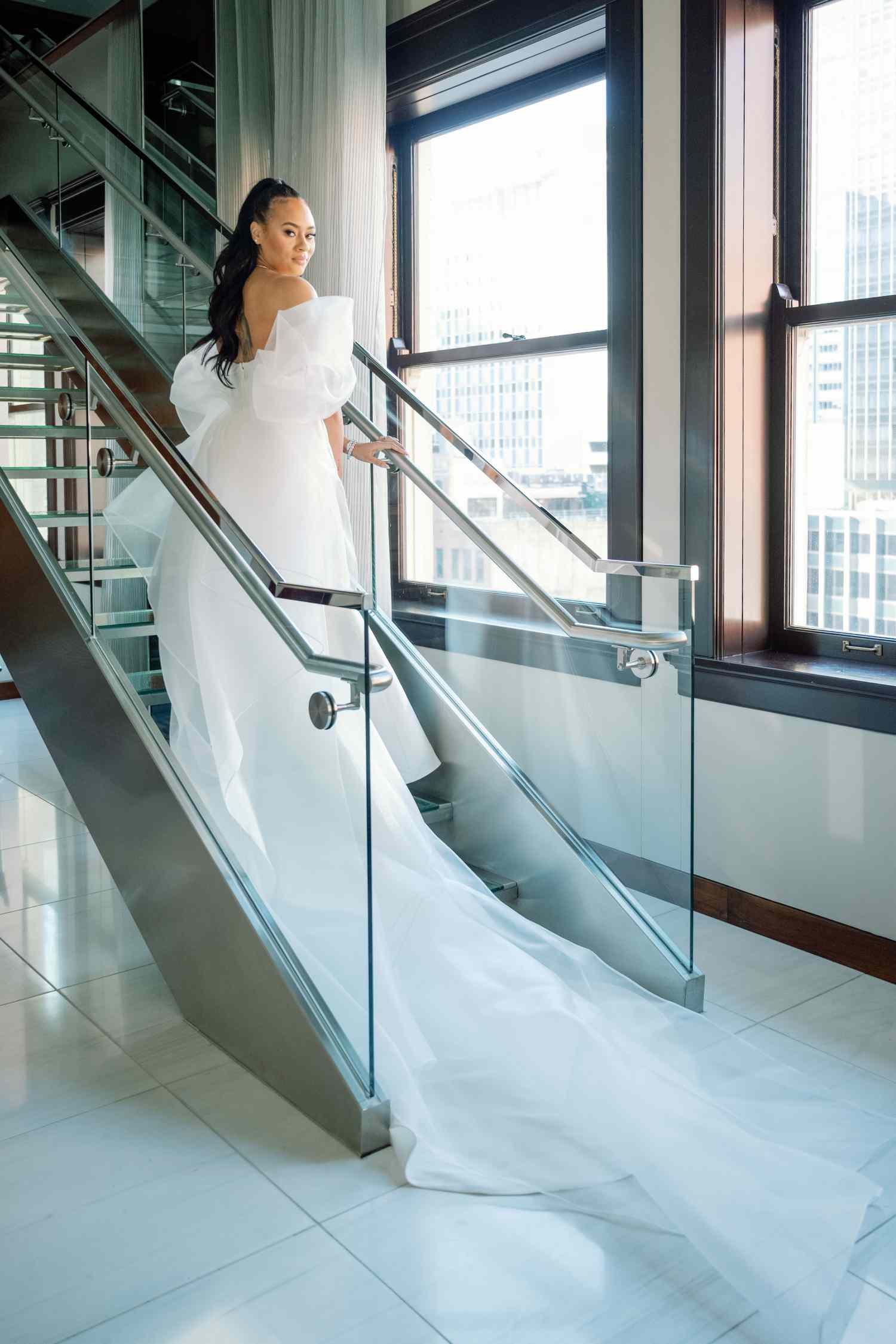 bride in white wedding gown looking over her shoulder on glass staircase