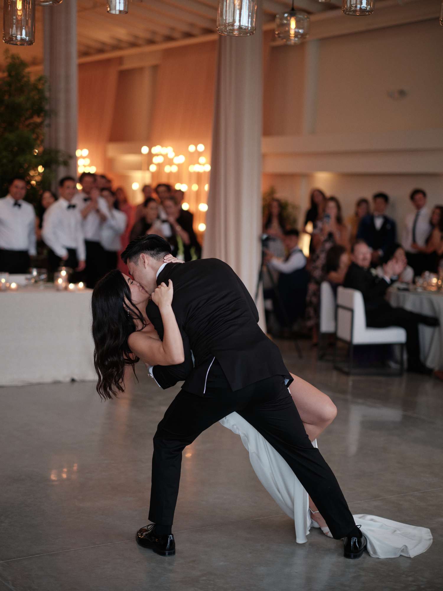 Bride in Wedding Dress Kissing Groom in Black Tuxedo on Dance Floor of Reception