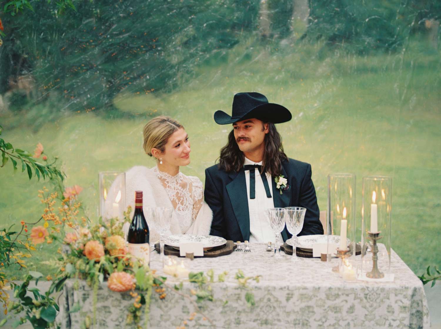 Bride in Lace Wedding Dress At Reception Main Table With Groom in Black Tuxedo and Western Hat