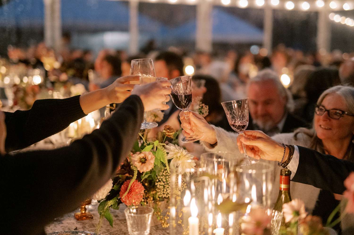 Guests Raising Cocktail Glasses in Candle Light at Reception Table