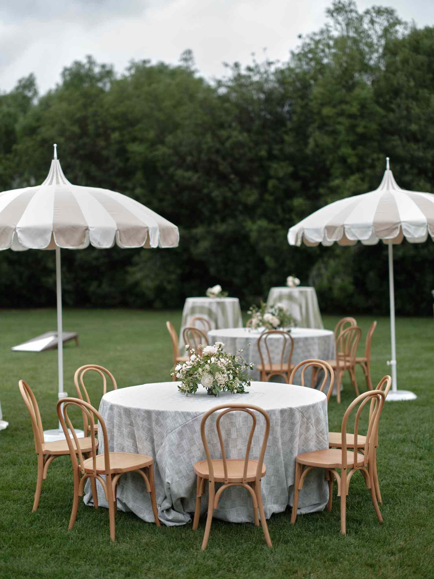 Round Tables With Wooden Chairs, White Flowers, and Umbrellas at Day After Wedding Party