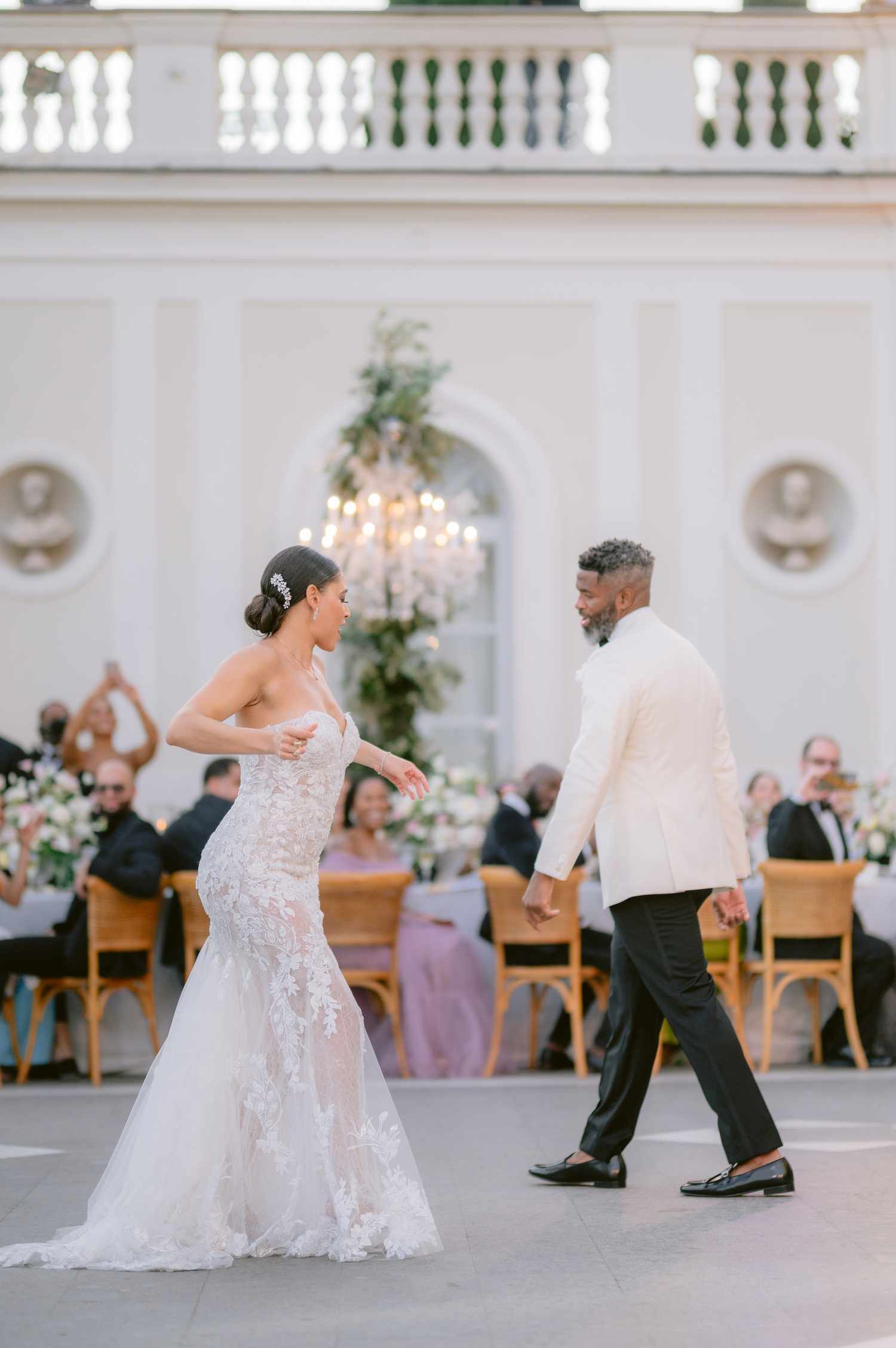 Bride in Lace Wedding Dress With Hair in Bun Dancing with Groom in Black and White Tuxedo