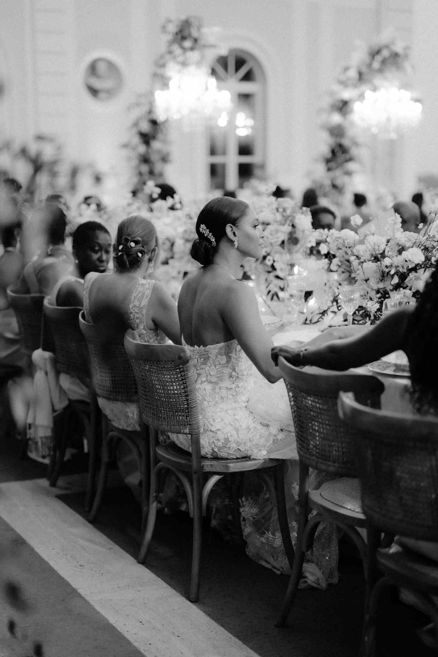 Black and White Image of Bride Seated with Guests at Reception Table