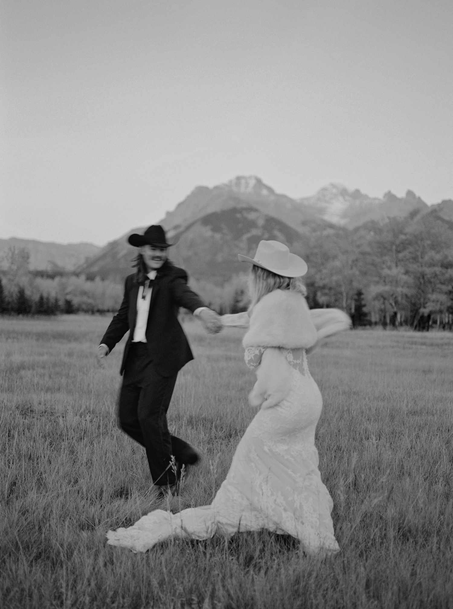 Black and White Portrait of Bride in Lace Wedding Dress and Western Hat Dancing With Groom in Black Tuxedo and Western Hat