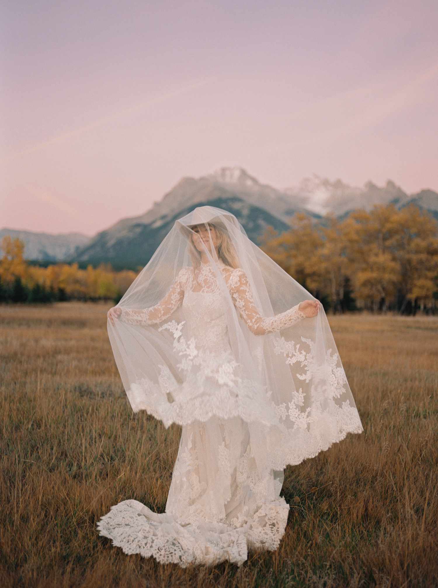 Portrait of Bride in Lace Wedding Dress and Veil With Western Hat in Grass Field