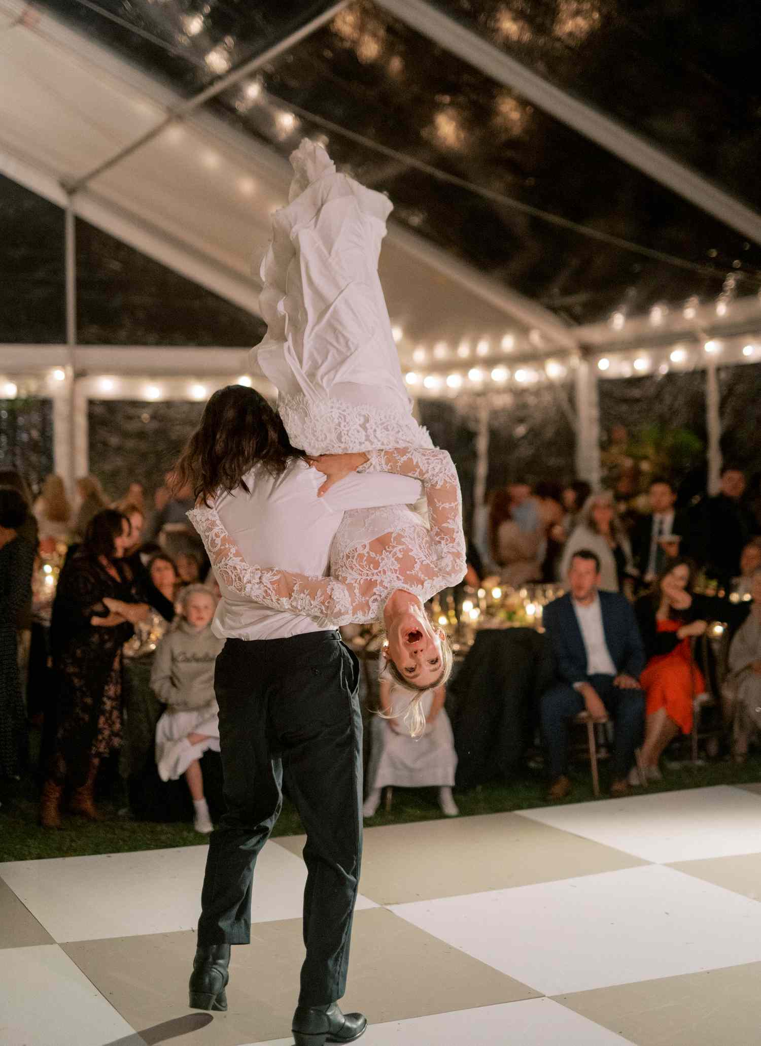 Groom Lifting Bride in Lace Wedding Dress Upside Down on Dance Floor at Wedding Reception