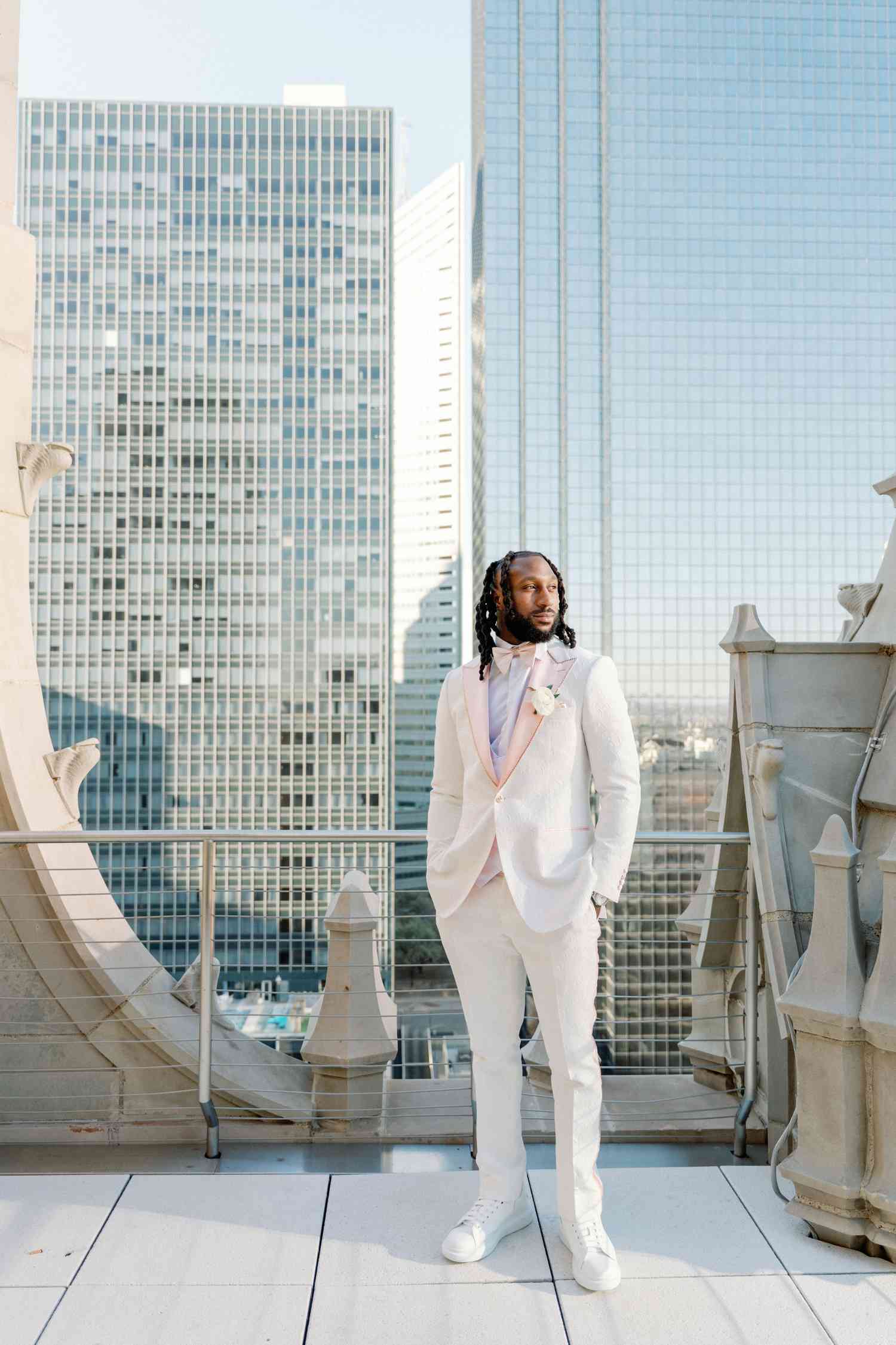 groom in white suit on a balcony with a city skyline view