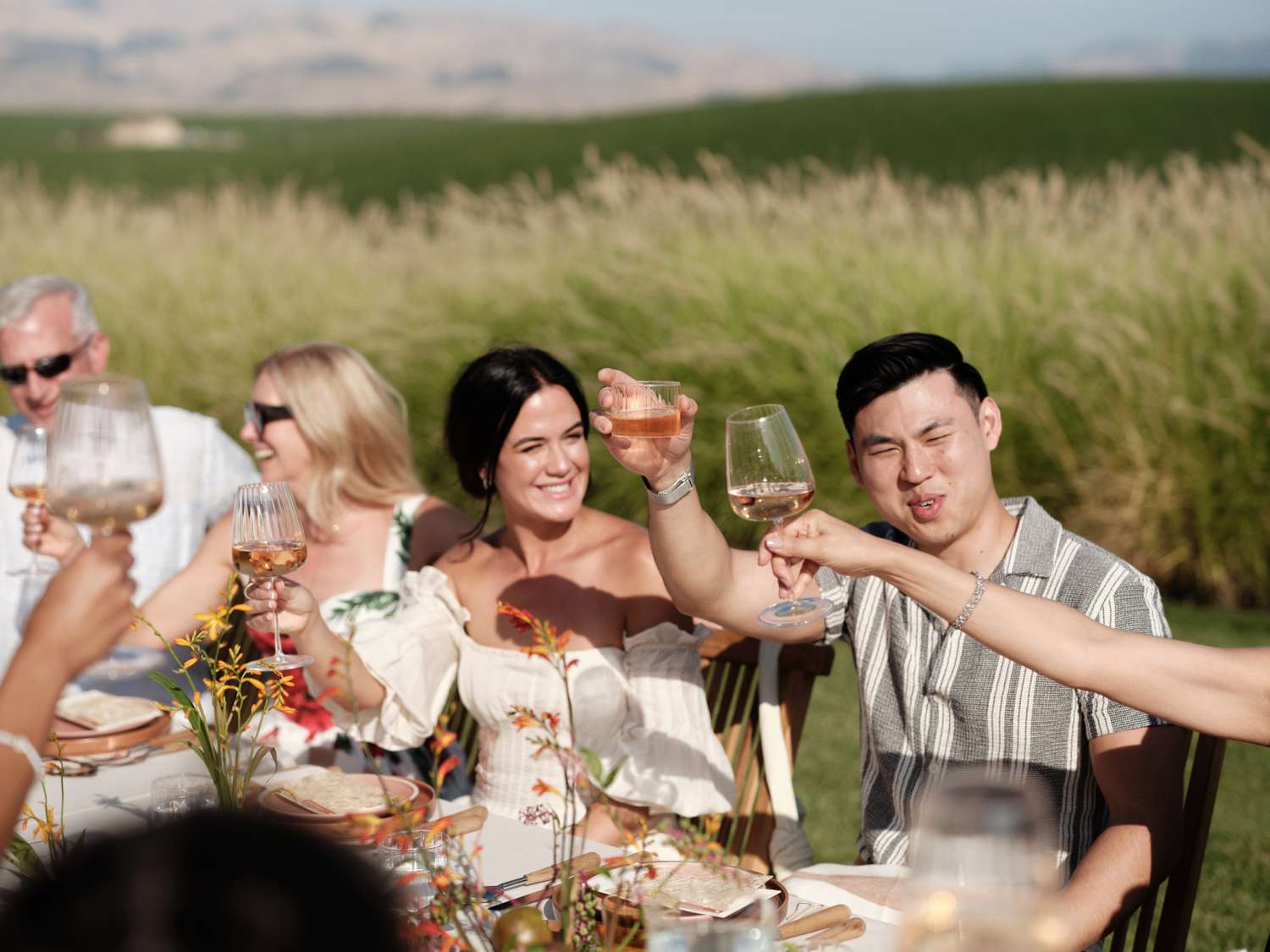 Bride in White Sundress Raising Glass With Groom in Stripped Shirt at Table