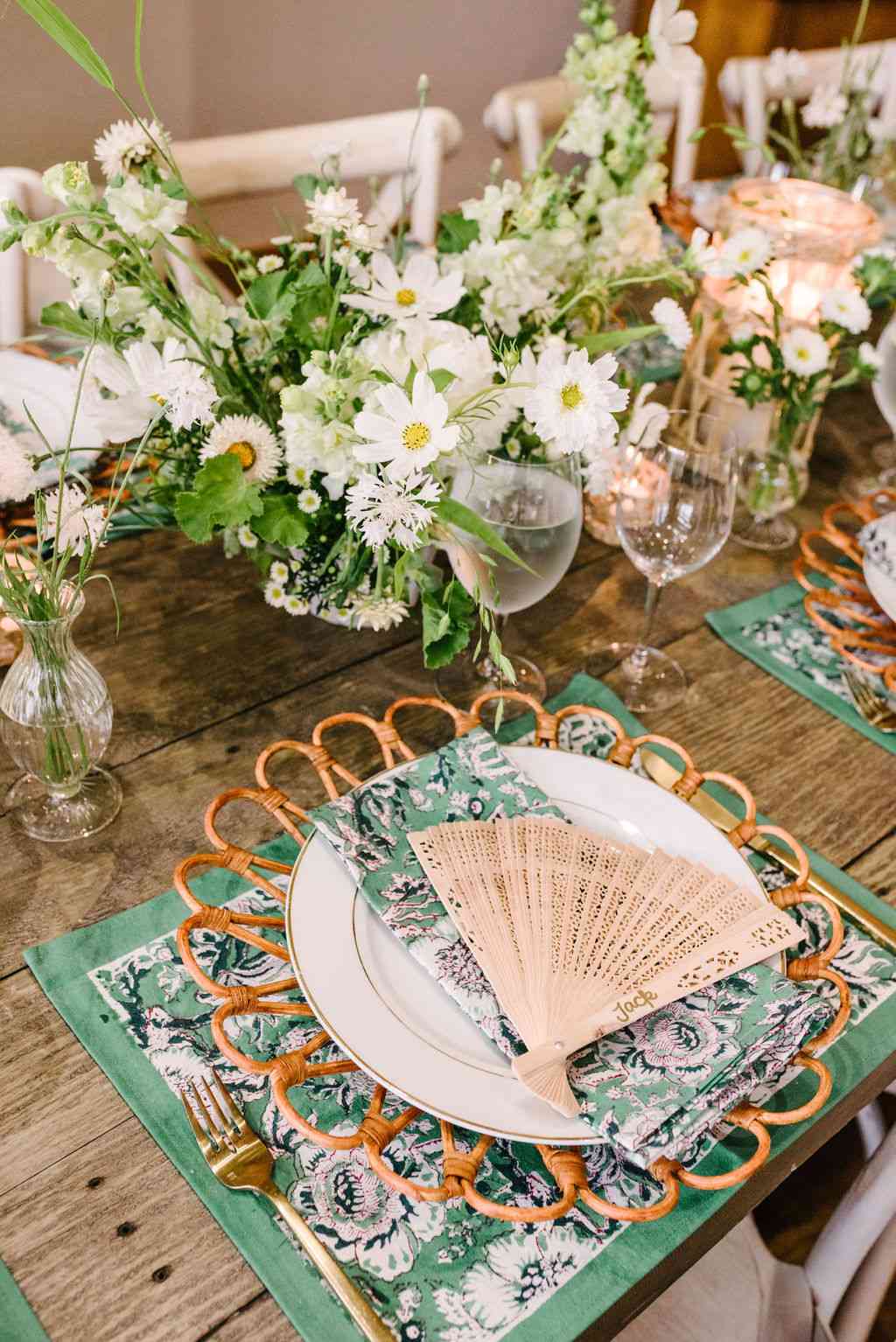 Wedding tablescape with florals, green printed linens, and customized fans