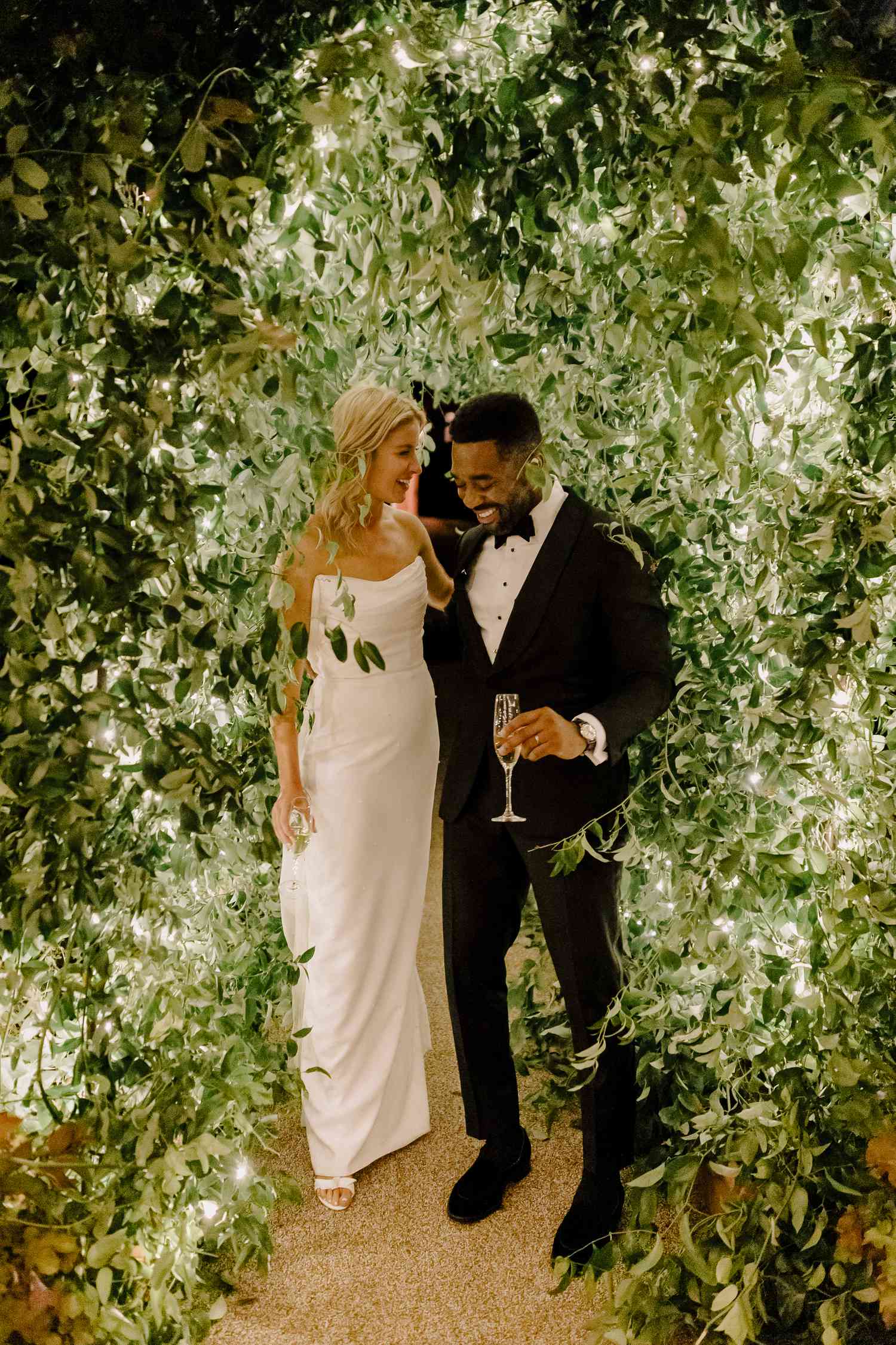 Bright and groom laughing while walking through a greenery tunnel