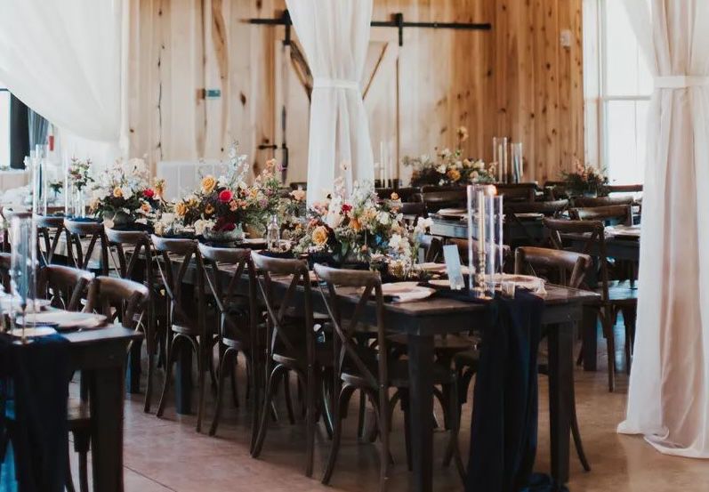 Wedding reception set up at Allenbrooke Farms with white curtains, black tables and chairs, and fresh flowers.