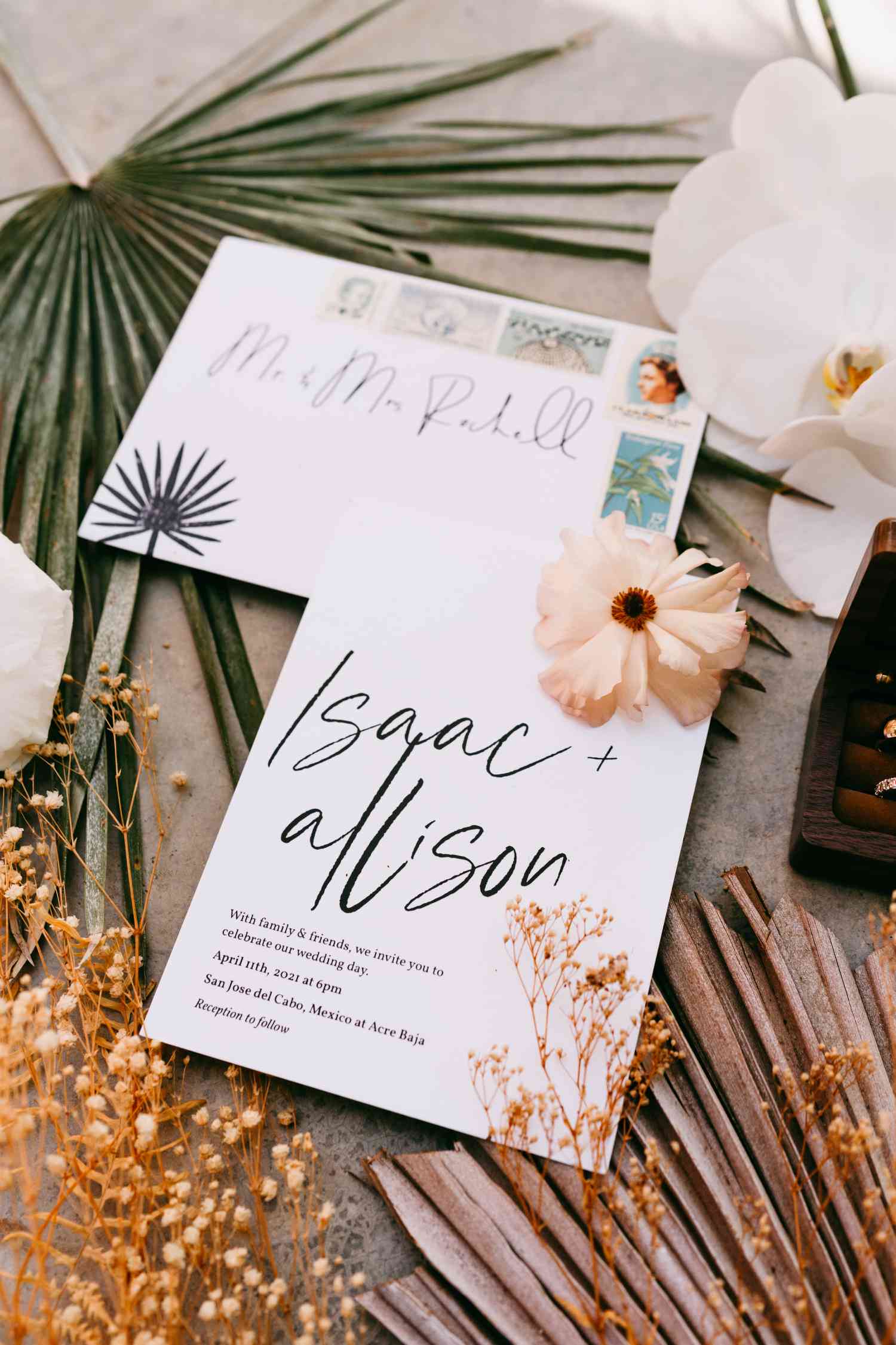 black and white Minimalist wedding invitation suite on flat lay with tropical flowers and palm fronds