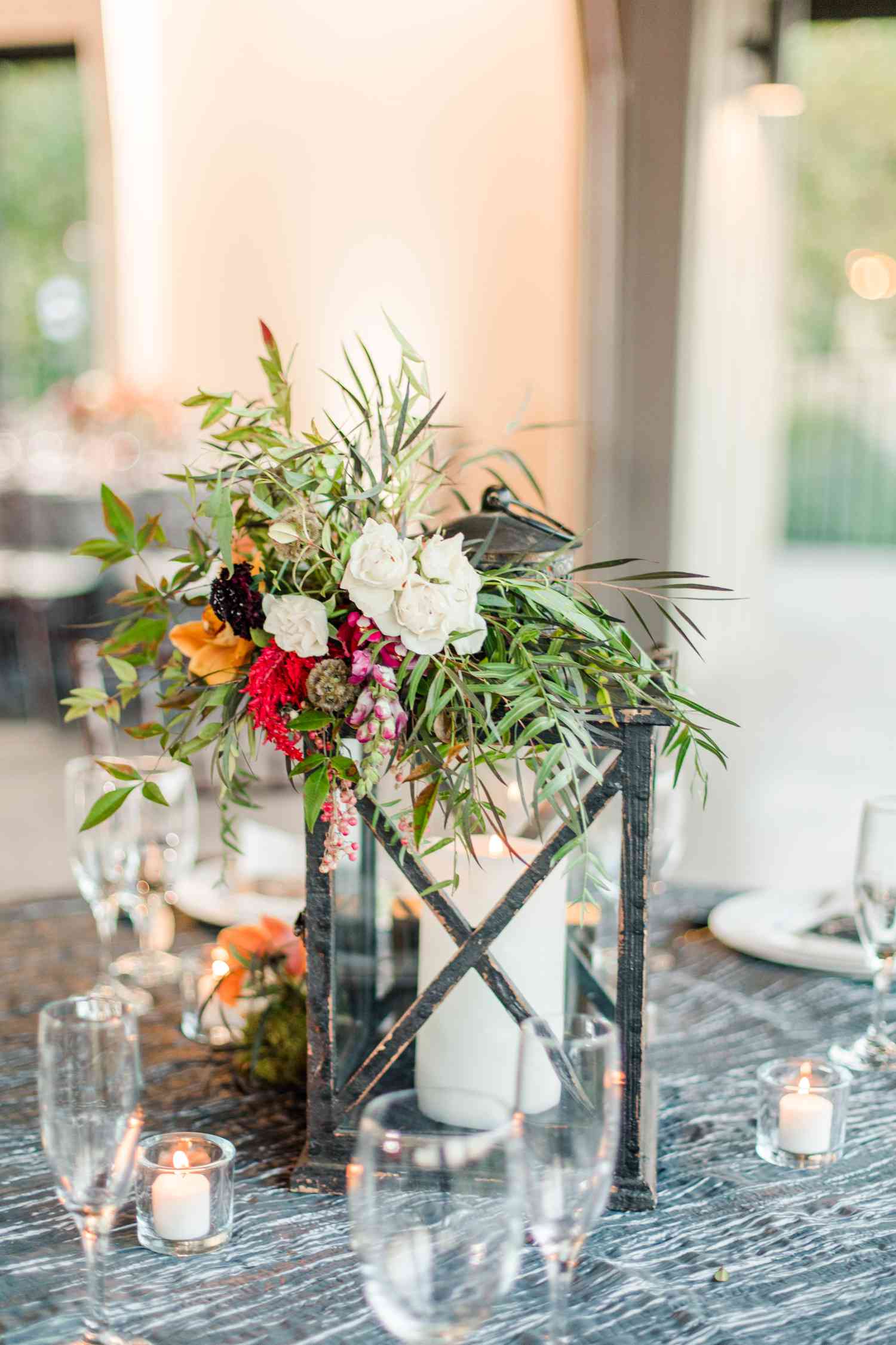 iron lantern topped with colorful flowers and greenery on a patterned tablecloth