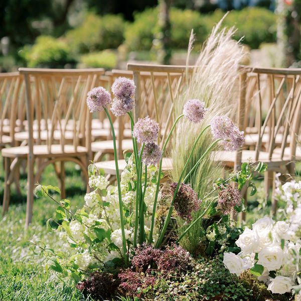 Cluster of Purple Alliums, Grasses, Dried Flowers, and White Roses Lining Wedding Aisle