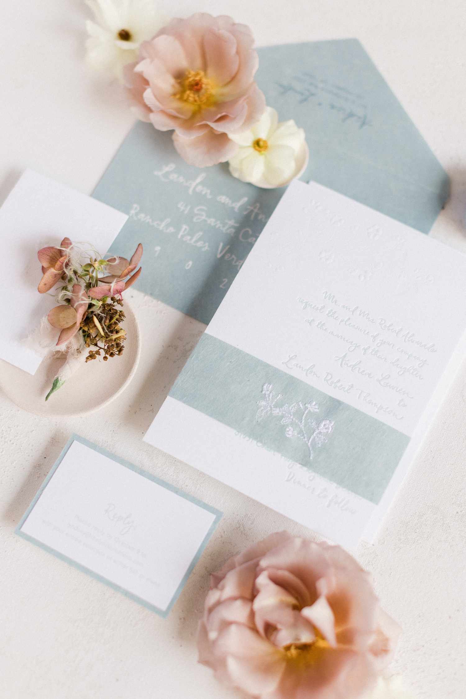 Light blue and white invitation suite with light blue band with floral design and additional florals