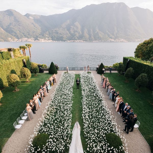 A waterfront wedding aisle with white flowers and a green lawn.