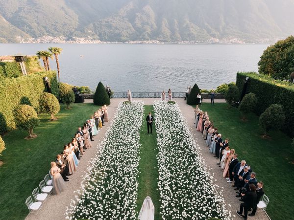 A waterfront wedding aisle with white flowers and a green lawn. 