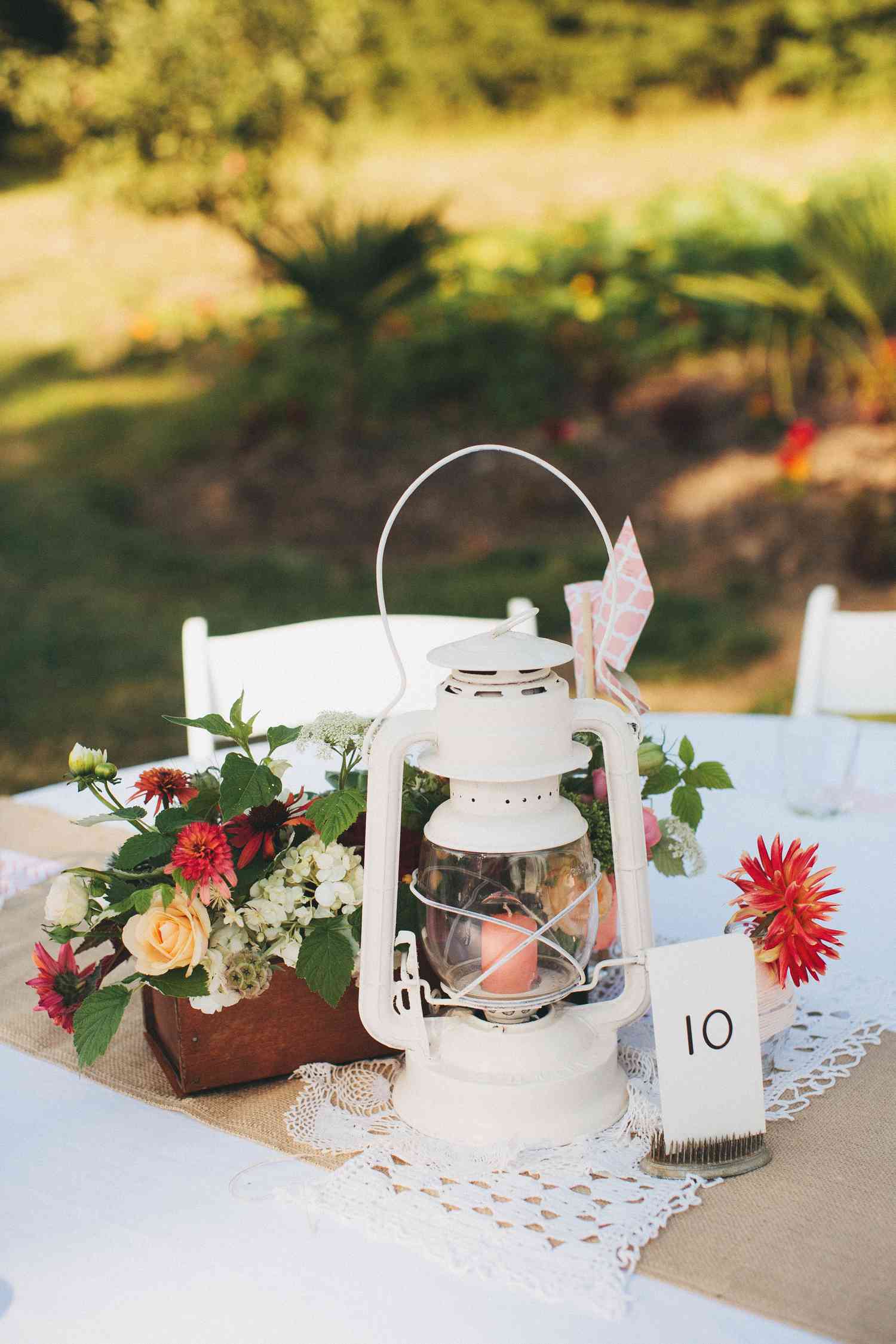 vintage white barn-style lantern on lace runner paired with wooden boxed of colorful flowers