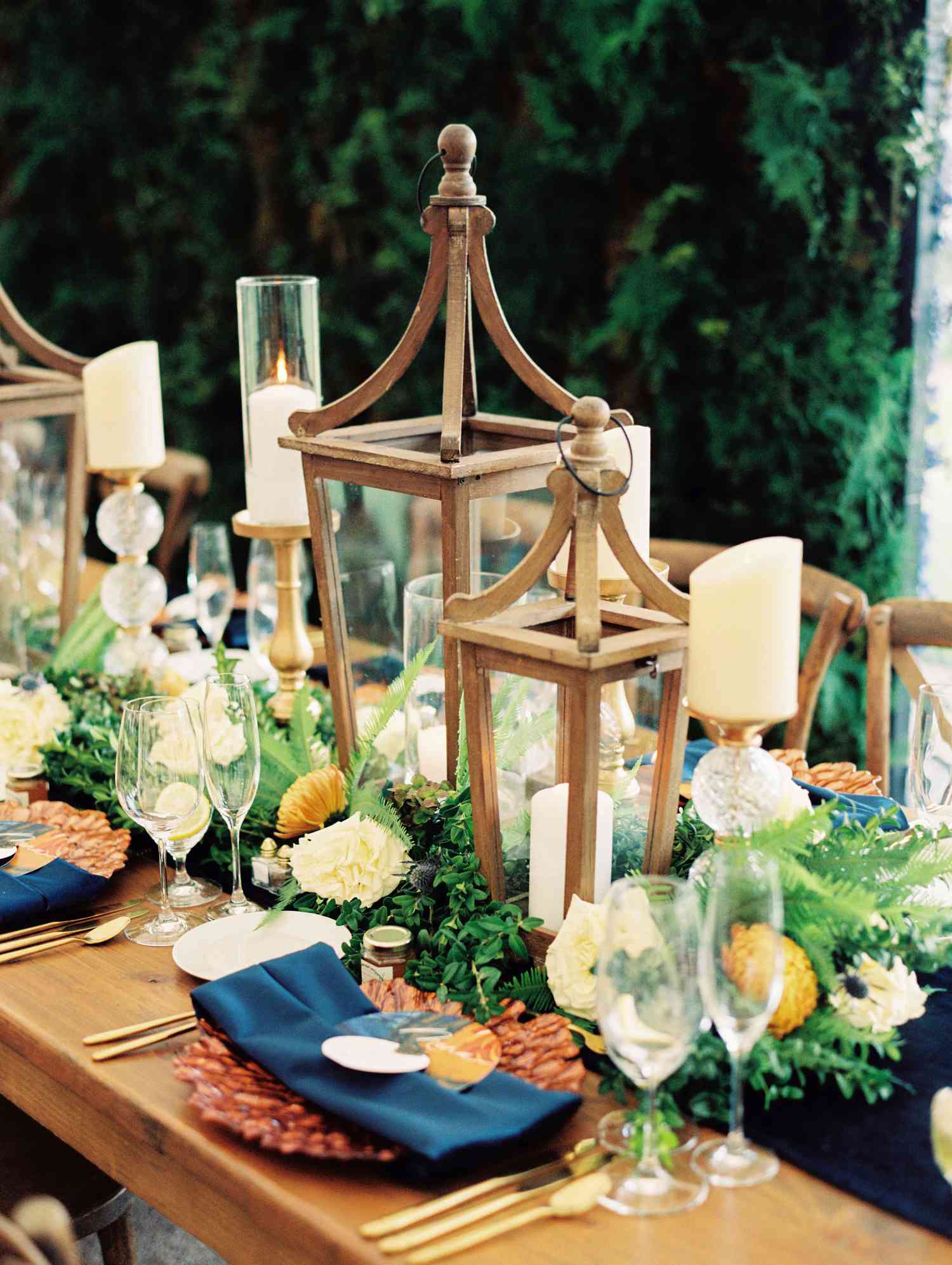 Wooden lanterns, votive candles on glass and gold holders, and place settings with blue napkins and textured plates
