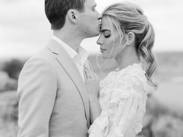 black and white photo of a man kissing his wife on her forehead 