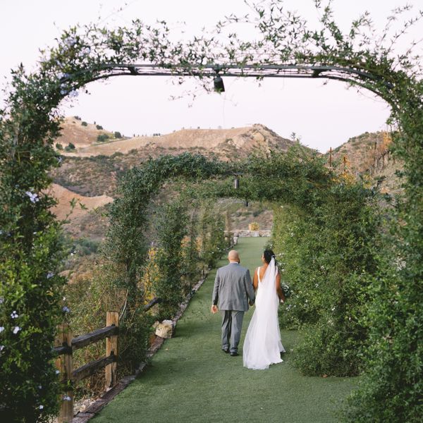Bride and groom walking hand-in-hand through arches covered in greenery during a destination wedding.