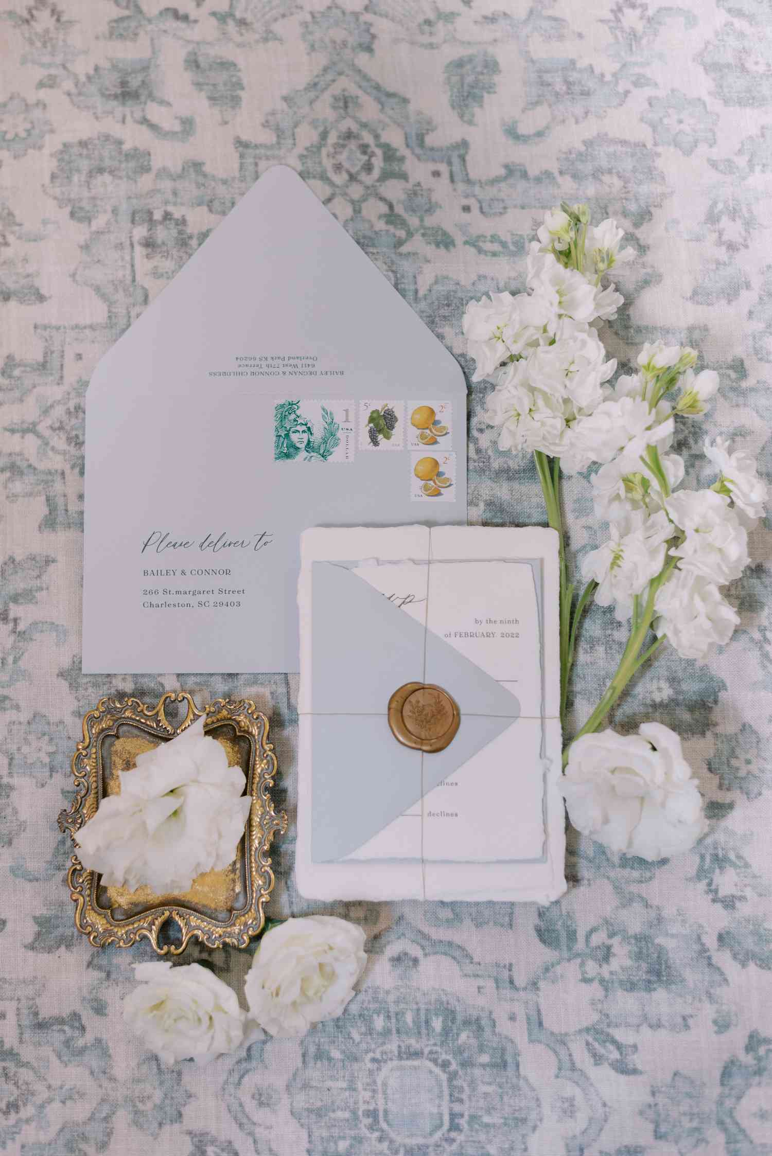 Blue and white invitation suite with gold wax seal and white florals on blue floral background