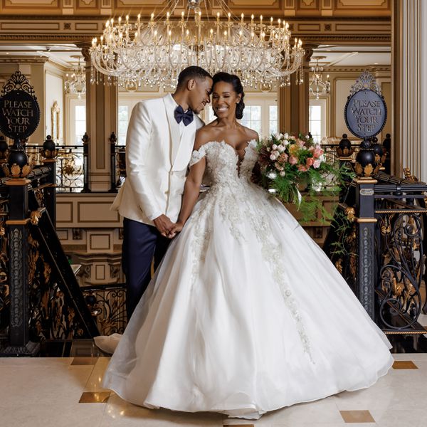 A regencycore wedding in a castle with a hanging chandelier behind the bride and groom