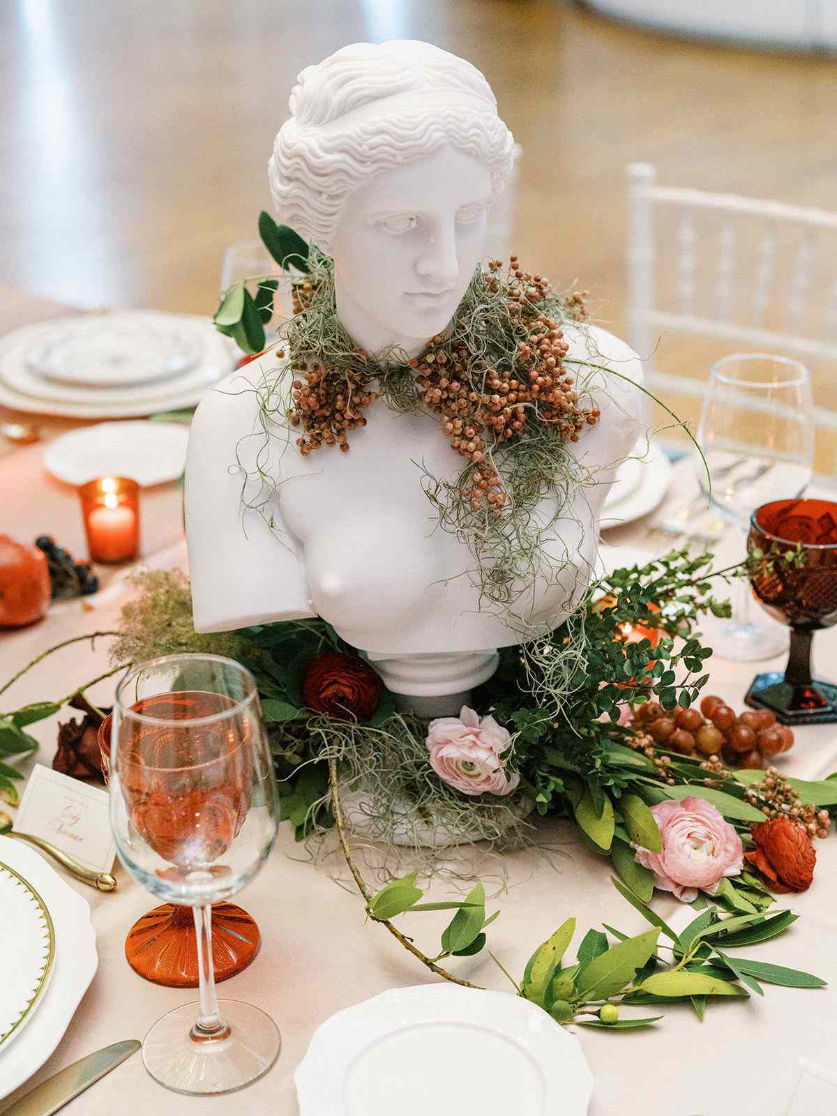 Bust centerpieces decorated with fruit and flowers on pink linens with red glassware