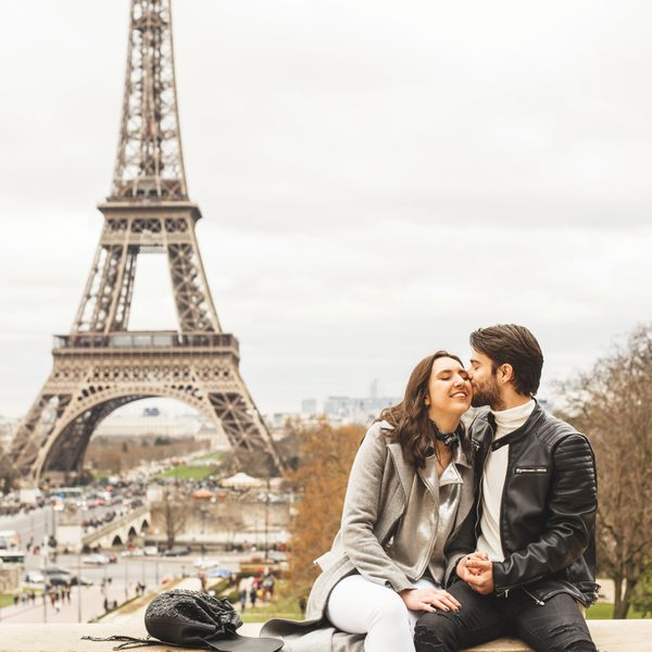 A man kissing a woman while sitting on a ledge in front of the Eiffel Tower in Paris