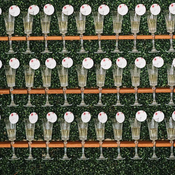 Champagne glass escort card display with round red and white cards on a greenery wall