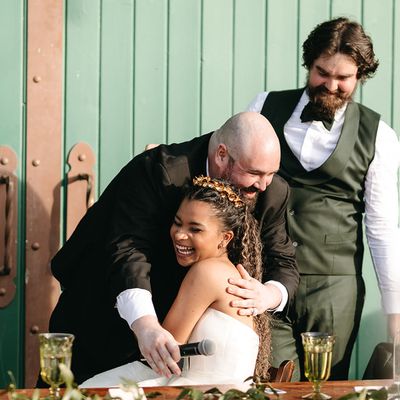 Best man hugs bride while standing next to groom after a best man speech at an outdoor wedding.