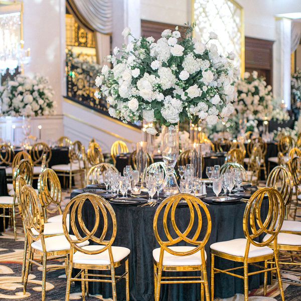 Round table with black velvet linens, gold chairs, and tall white floral centerpieces