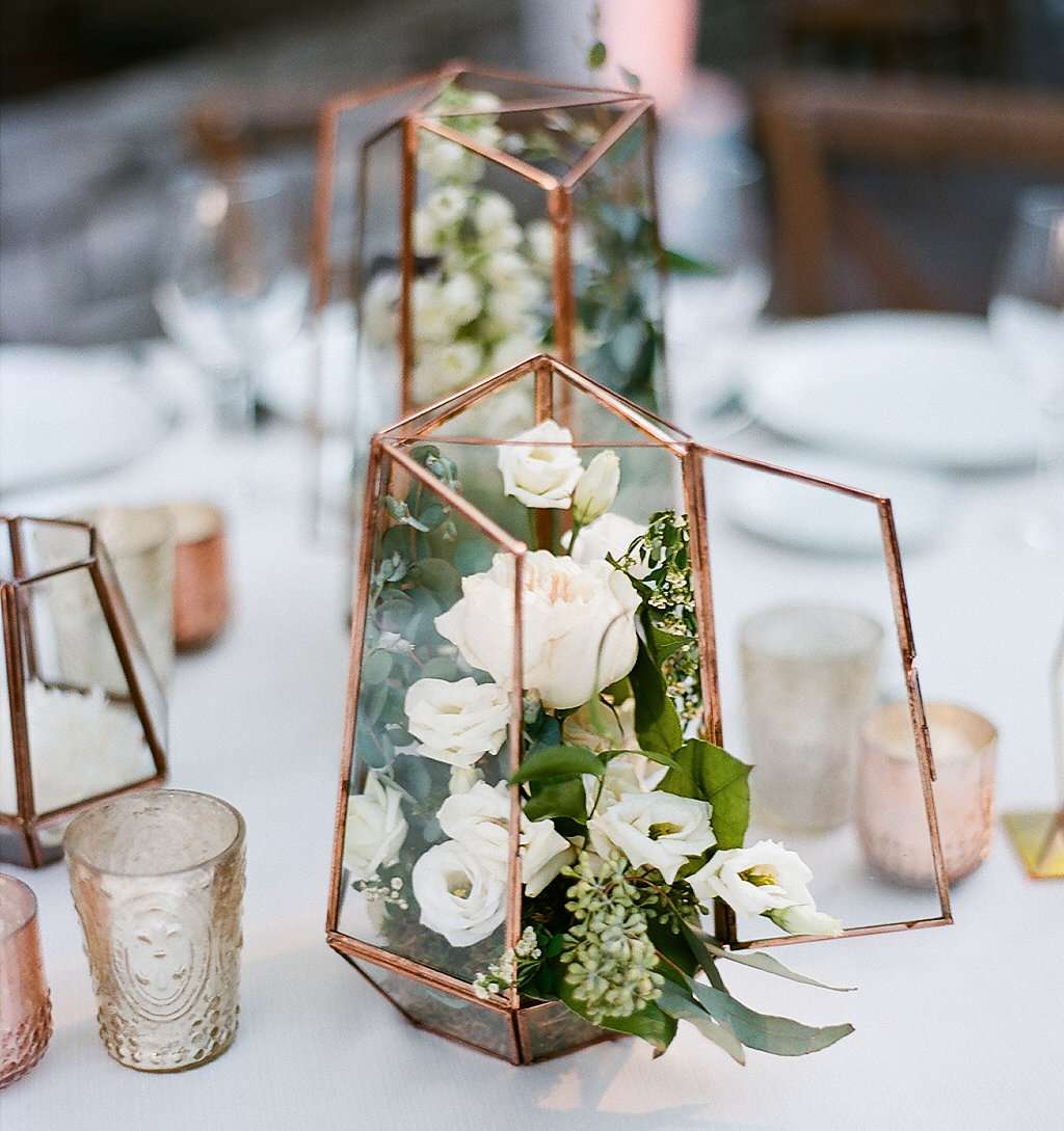 rose gold lantern stuffed with white flowers and greenery on white linens