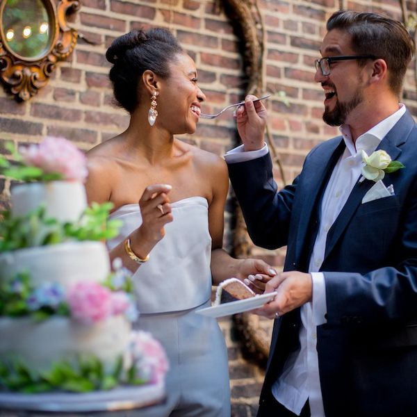 A bride in a white dress and groom in a blue formal suit cutting their floral cake at their wedding.