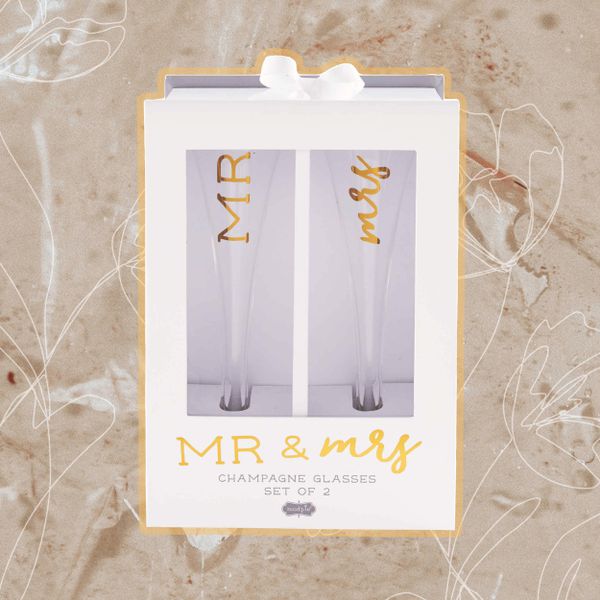 Mud Pie Mr. & Mrs. Champagne Glass Set displayed on a textured background with a floral sketch overlaid