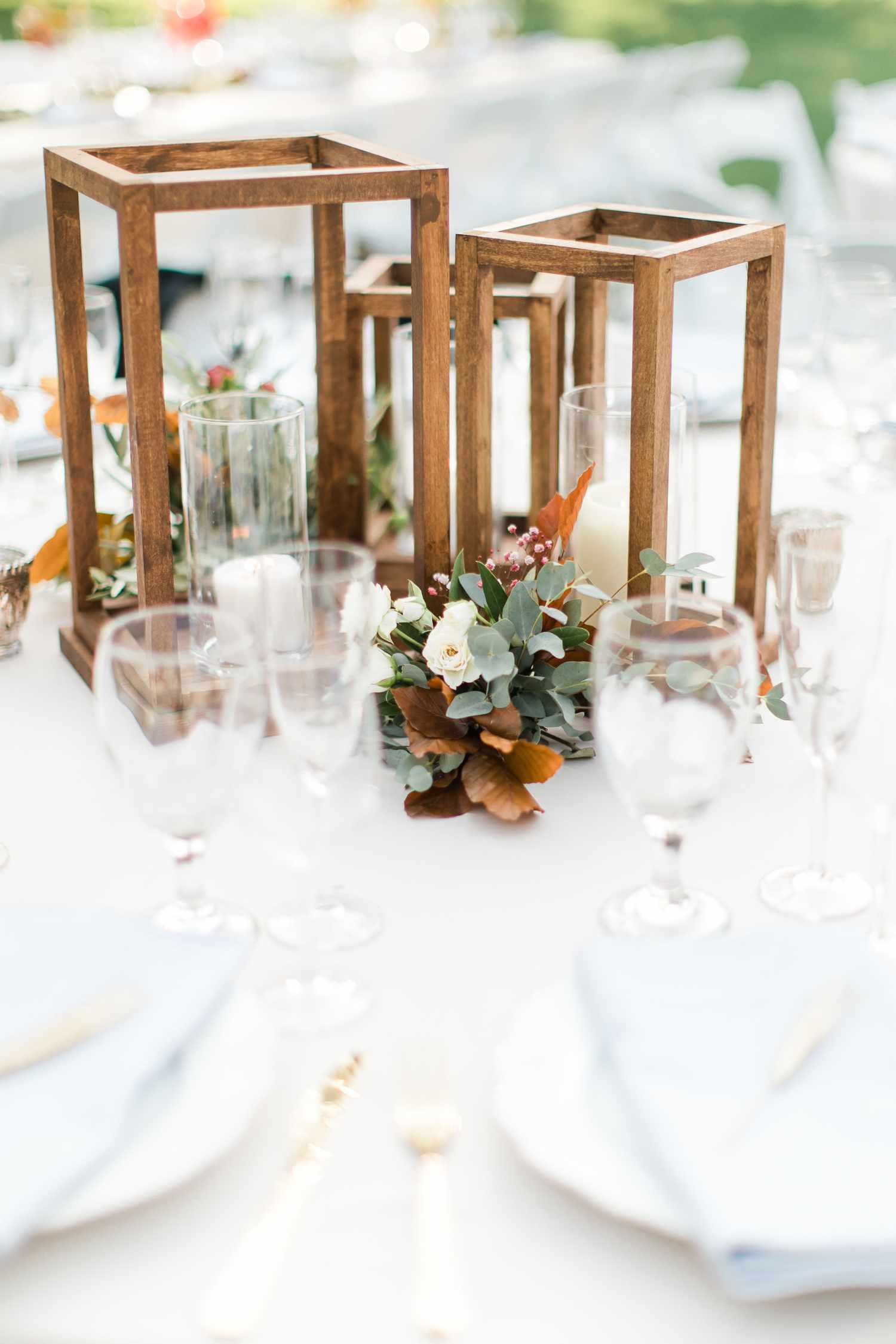 Trio of wooden lanterns in various sizes on white linens with fall-like flowers