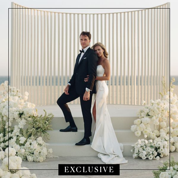 Dallas Stars Goaltender Jake Oettinger in Black Tuxedo and Bride in Wedding Dress With High Slit Standing in Front of Modern Ceremony Structure With White Flowers on the Beach