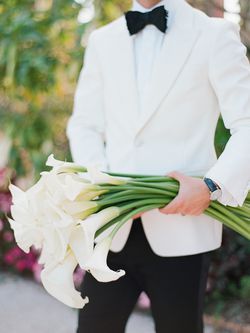 groom wearing a tuxedo holding a bouquet of calla lilies 