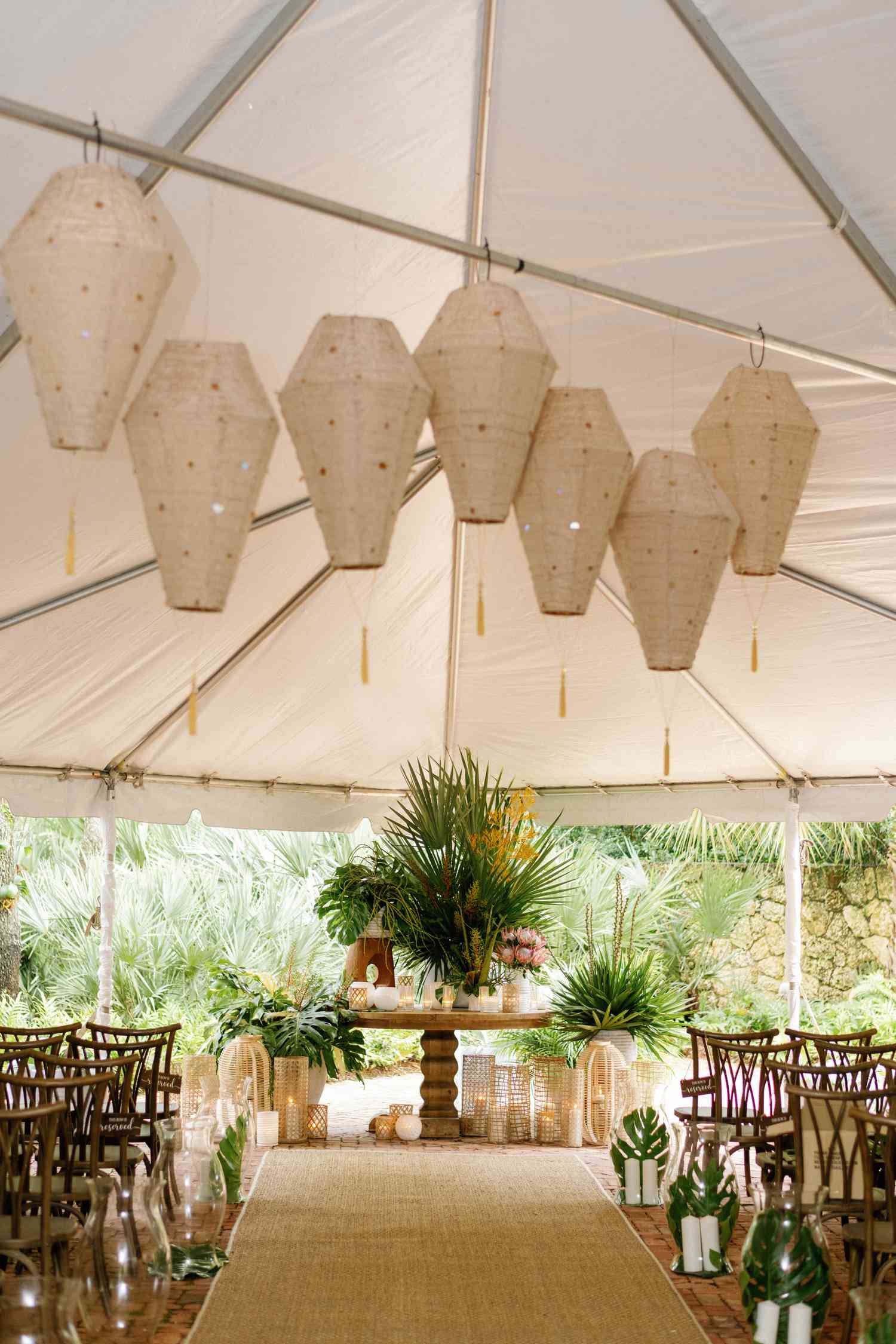Ceremony setup with paper lanterns, rattan lanterns, monstera leaves, pillar candles, palm leaves