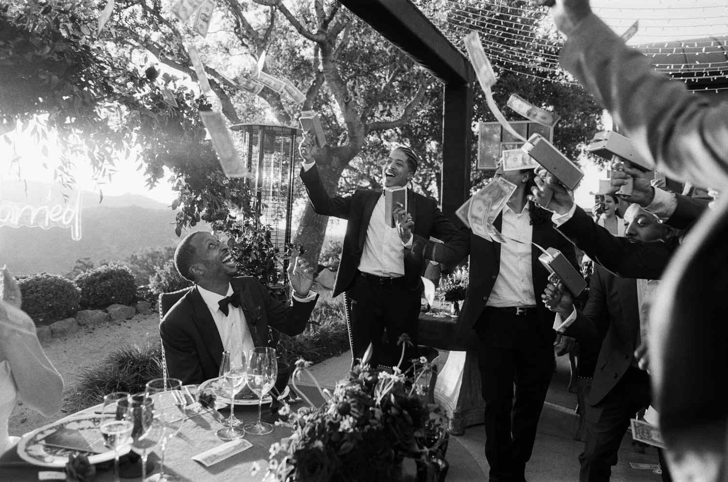 Guests Throwing Money at Couple Sitting at Dinner Table Outside
