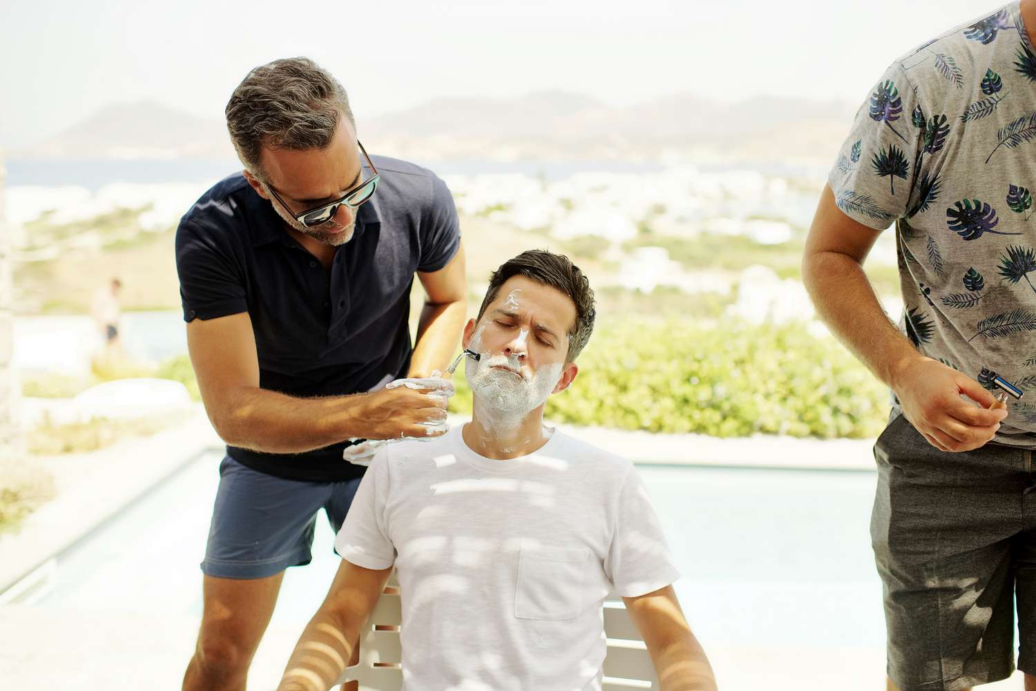 Groom sitting on deck overlooking Greece island while getting a shave