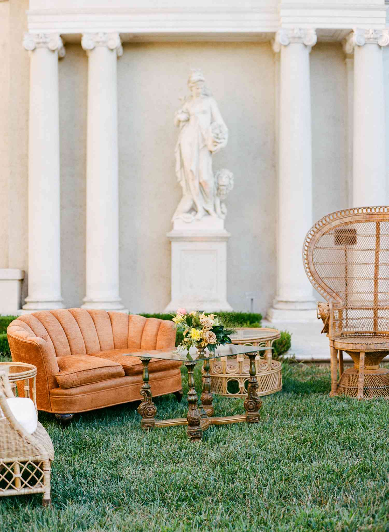 Outdoor Lounge Area With Orange Velvet Couch, Wicker Furniture, and Antique Coffee Table
