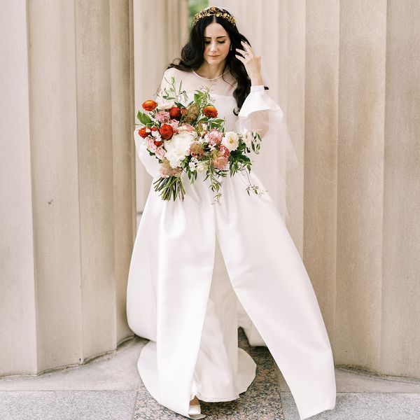 a bride holding a bouquet of red, white, and pink flowers, while wearing a long-sleeve wedding gown and gold tiara