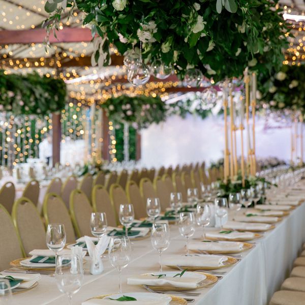 Banquet Table With White Linens, Glassware, Place Settings, and Tall Greenery Installation With Hanging Tea Lights