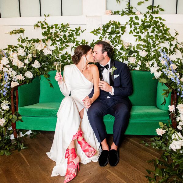 Bride and groom kissing on velvet green couch surrounded by flowers and greenery