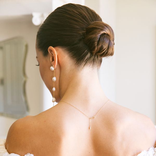 Back of Brunette Bride With Low Bun Hairstyle, Low Back Dress, and Pearl Earrings
